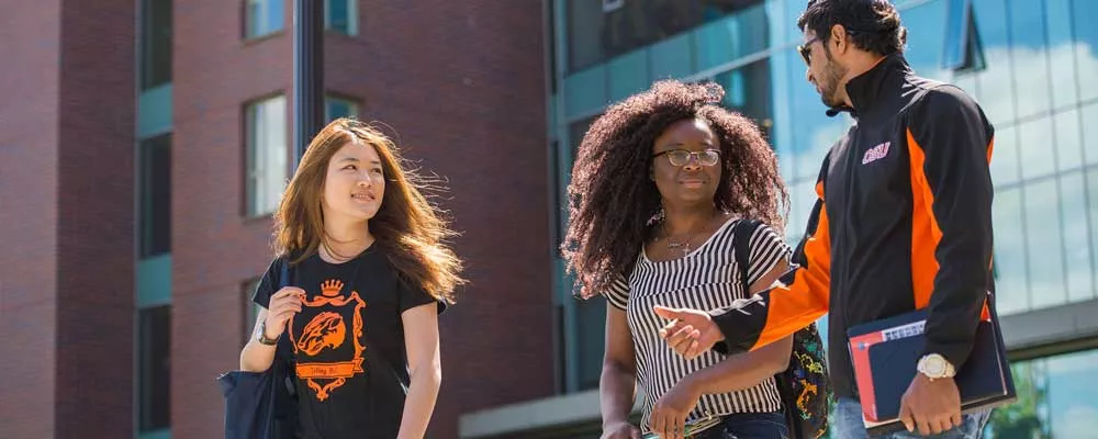 three students wearing OSU clothing and carrying books walking and talking